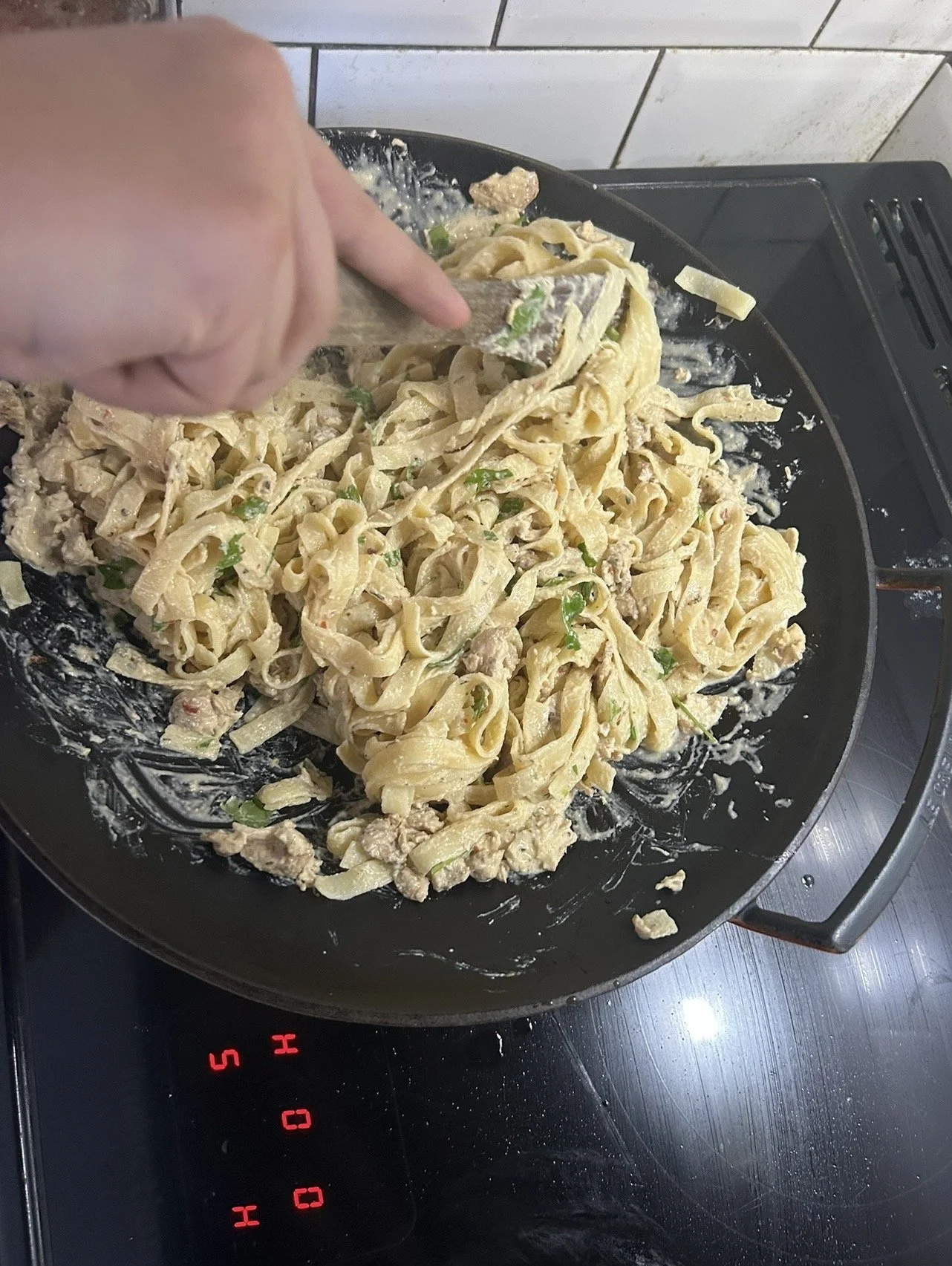 Cooking pasta with chicken and green onions in a black frying pan on an electric stovetop.