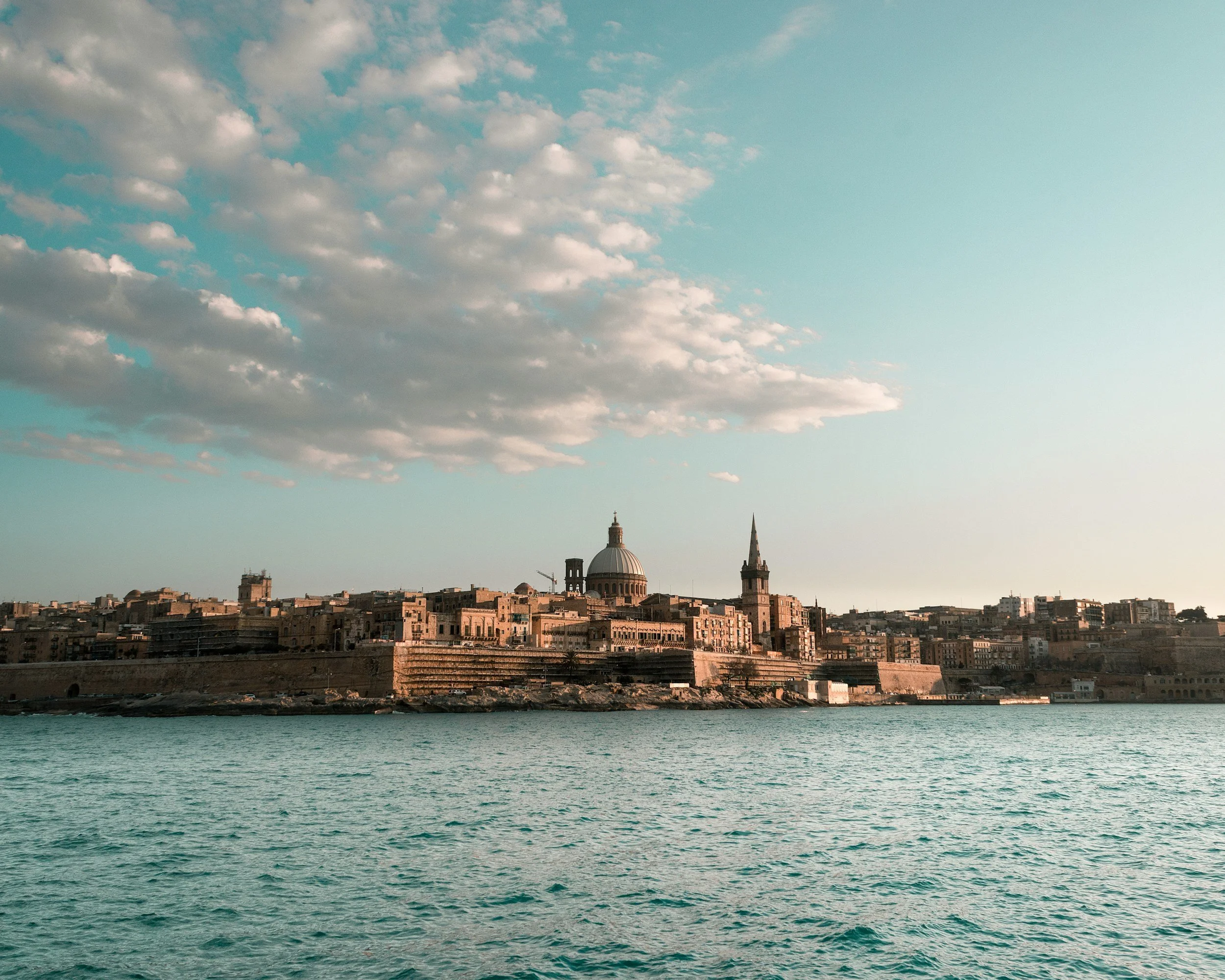 View of the city of Valletta, Malta, from across the water with a cloudy sky overhead.
