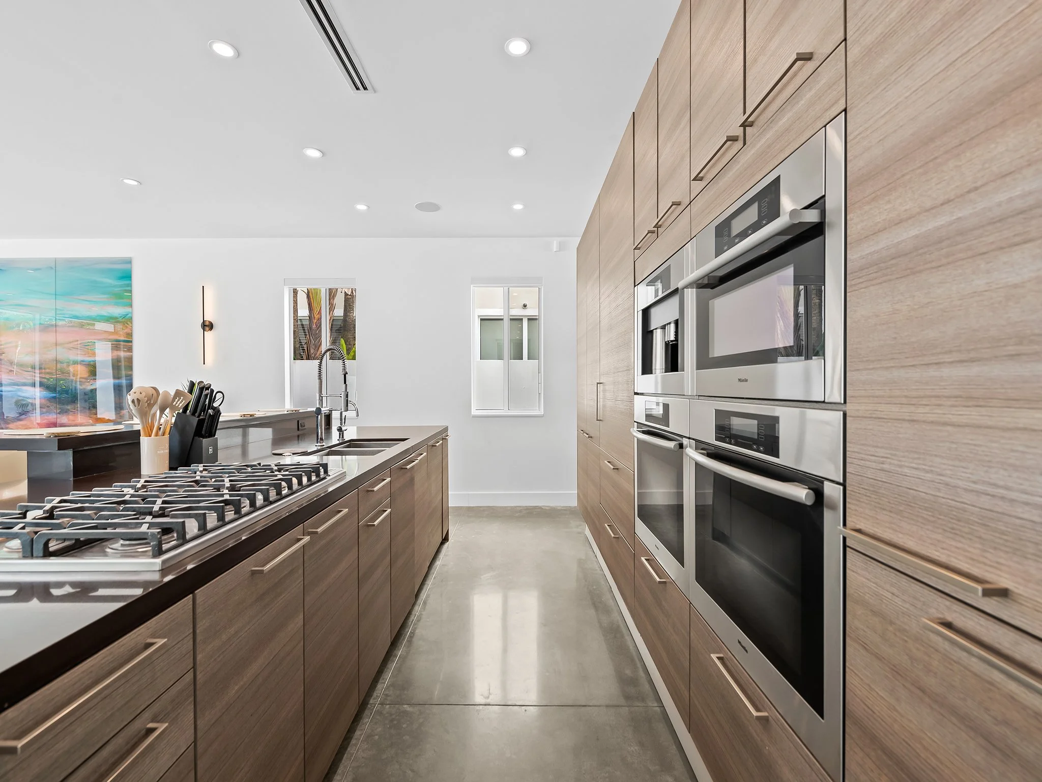 Modern kitchen with wood cabinets, stainless steel appliances, a stove with gas burners, a kitchen island, and a painting on the wall.