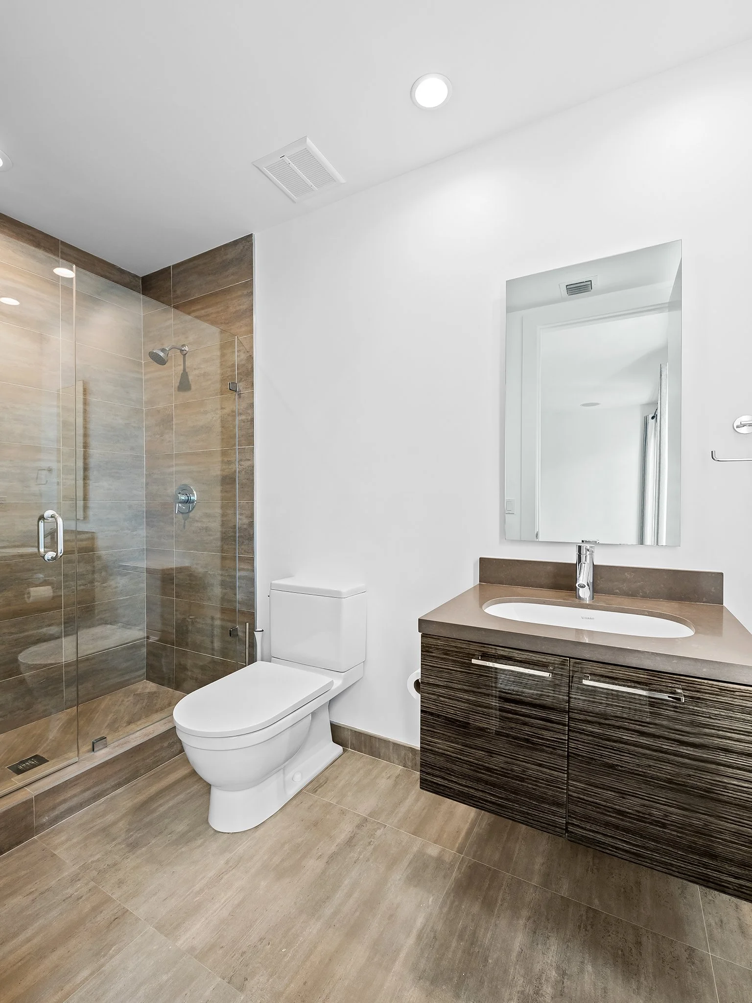 Modern bathroom with a glass-enclosed shower, white toilet, wooden vanity with sink, mirror, and recessed ceiling lights.