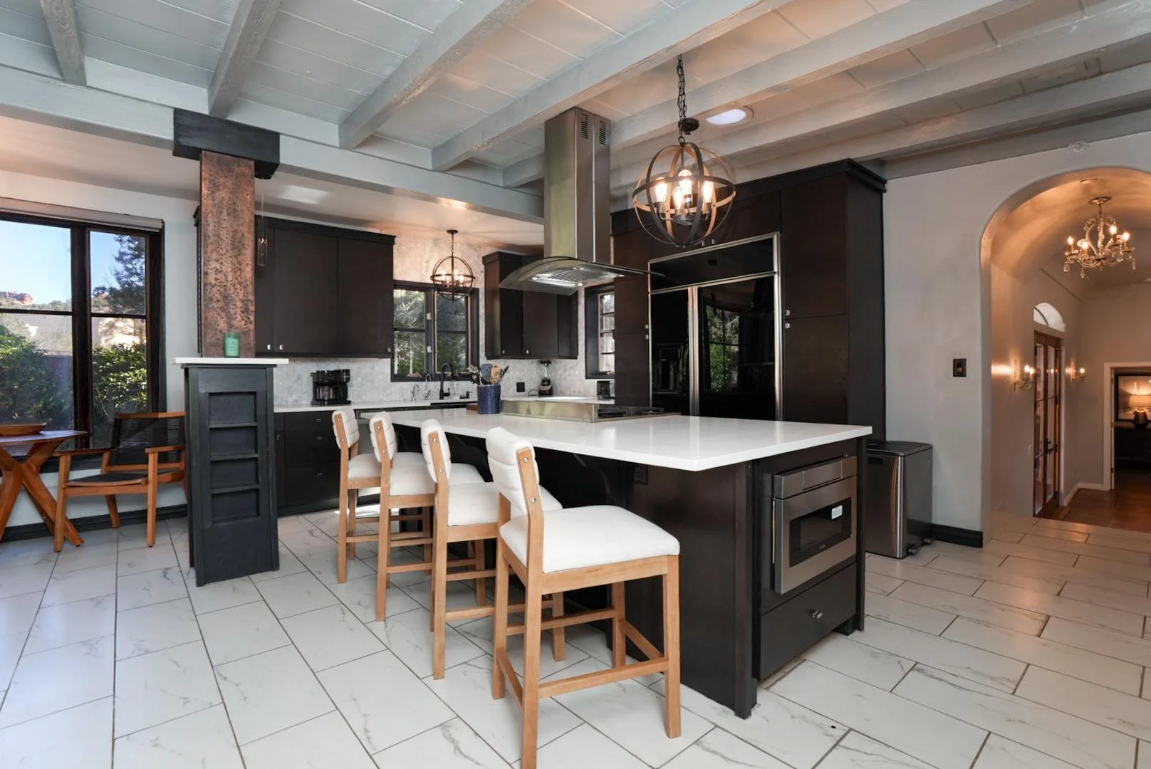 Modern kitchen with black cabinets, white countertop island, chandelier lighting, and large tiled floor.