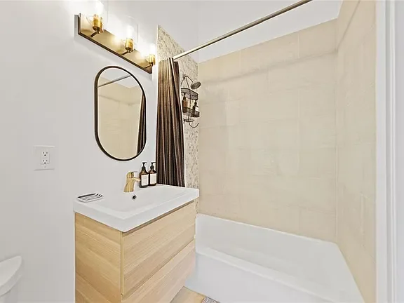 Bathroom with a vanity, mirror, and a shower with beige tiles