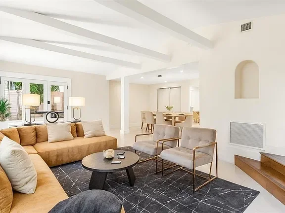 Living room with beige sofa, two beige armchairs, black coffee table, black area rug, and large windows with white curtains.