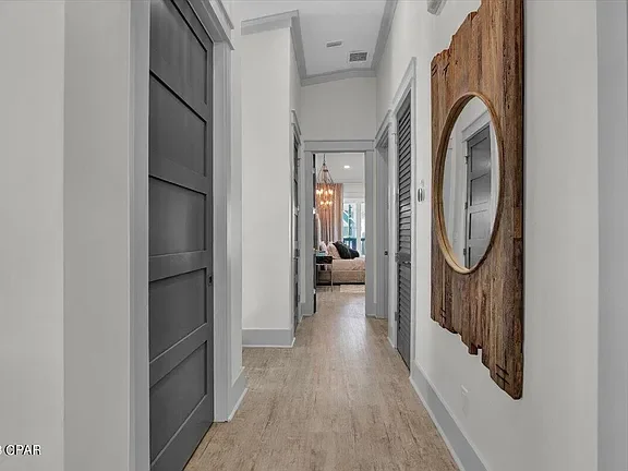 Hallway with white walls, light wood flooring, gray paneled doors, and a wooden wall mirror on the right