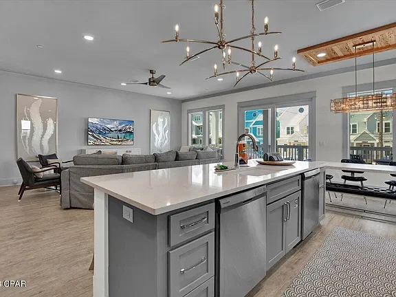 Modern open-concept living room and kitchen with gray cabinetry, white countertops, a chandelier, and large windows.