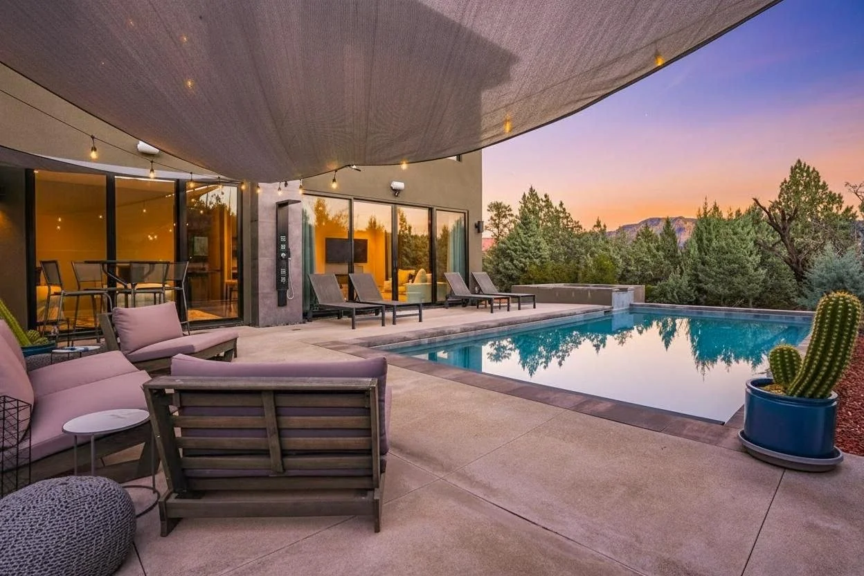 Modern backyard with a pool, outdoor seating, and a view of trees and mountains at sunset.