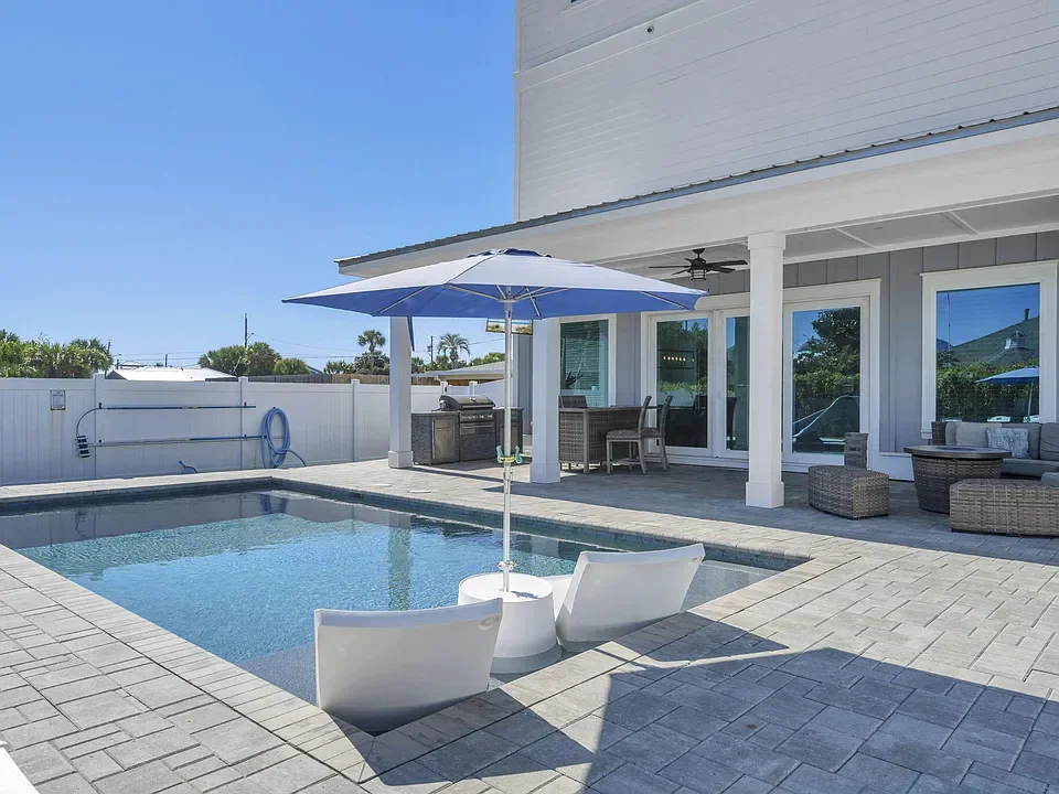 Backyard with a swimming pool, outdoor seating, a patio umbrella, and a covered patio area with furniture.
