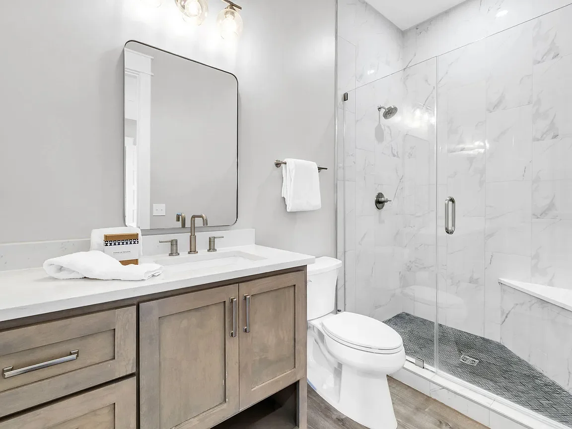 Modern bathroom with a vanity, mirror, towel rack, toilet, and walk-in shower with glass door and marble walls.