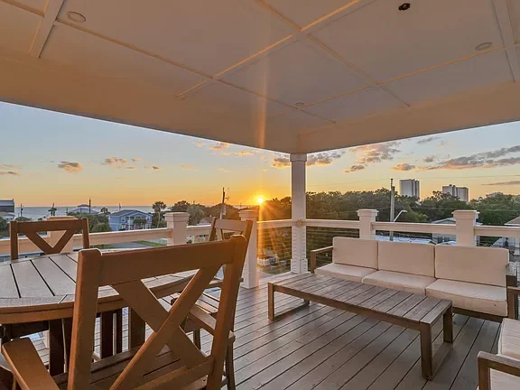 Sunset view from a balcony with outdoor furniture, including a table, chairs, and a white sofa.
