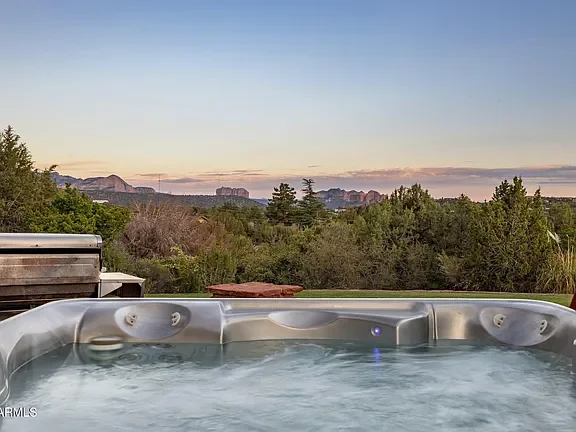 Hot tub with water jets on an outdoor deck overlooking a landscape of trees and distant mountains at sunset.