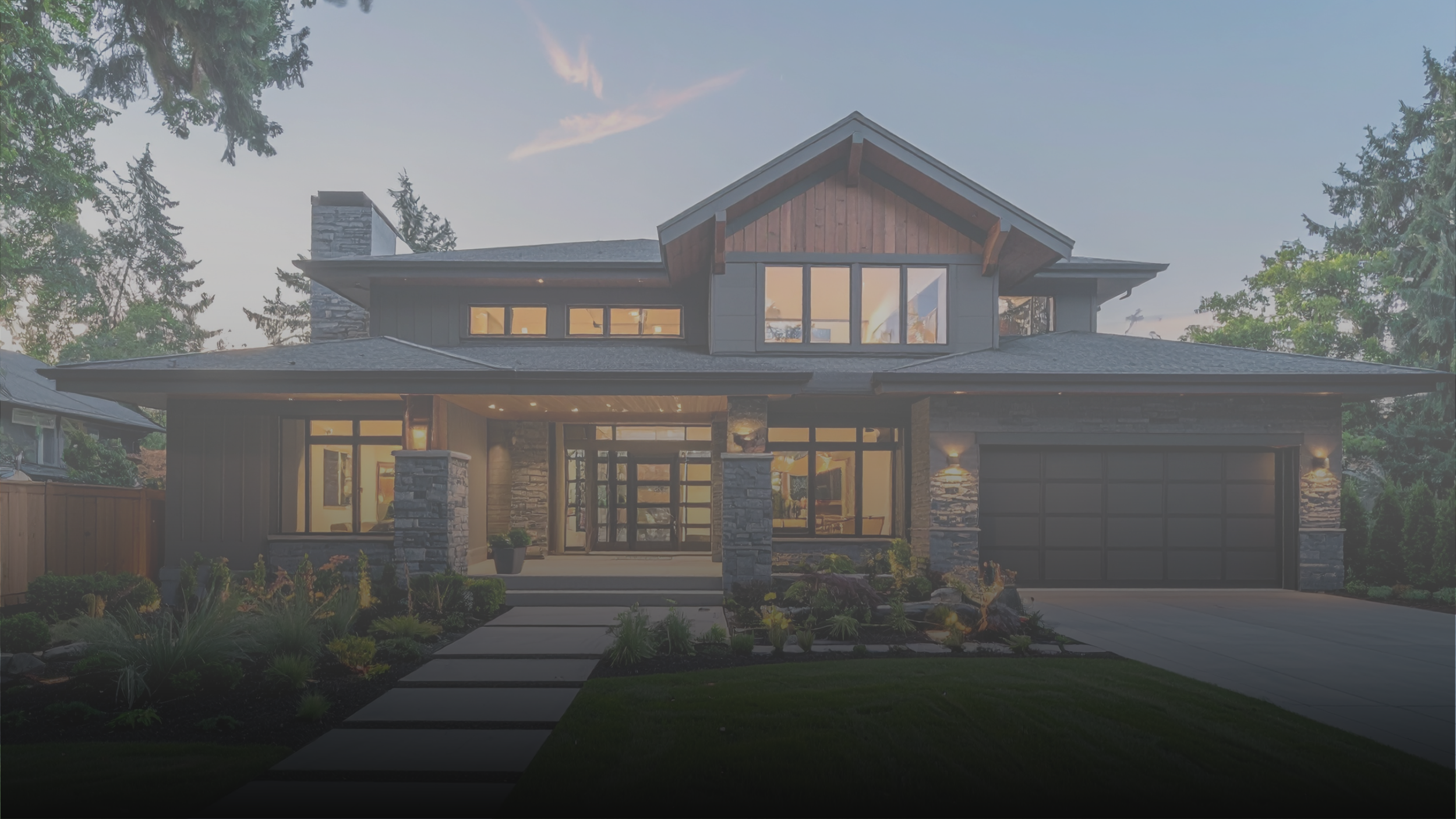 Modern two-story house with a stone and wood exterior, large front windows, a garage, and landscaped front yard with pathway and garden plants, during dusk.