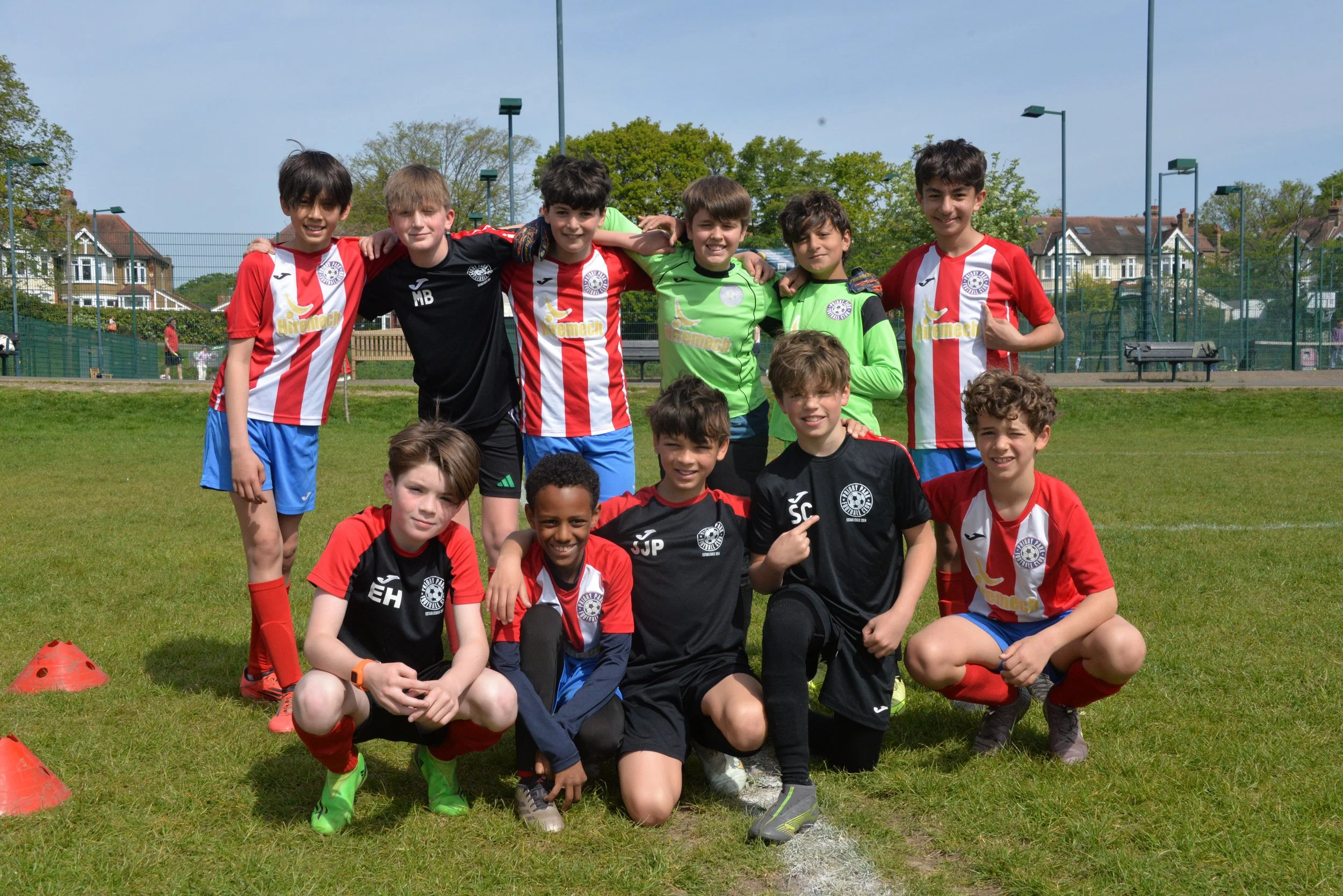 A group of young boys and girls in soccer uniforms posing on a grass field after a game or practice, with some kneeling and others standing, smiling at the camera.