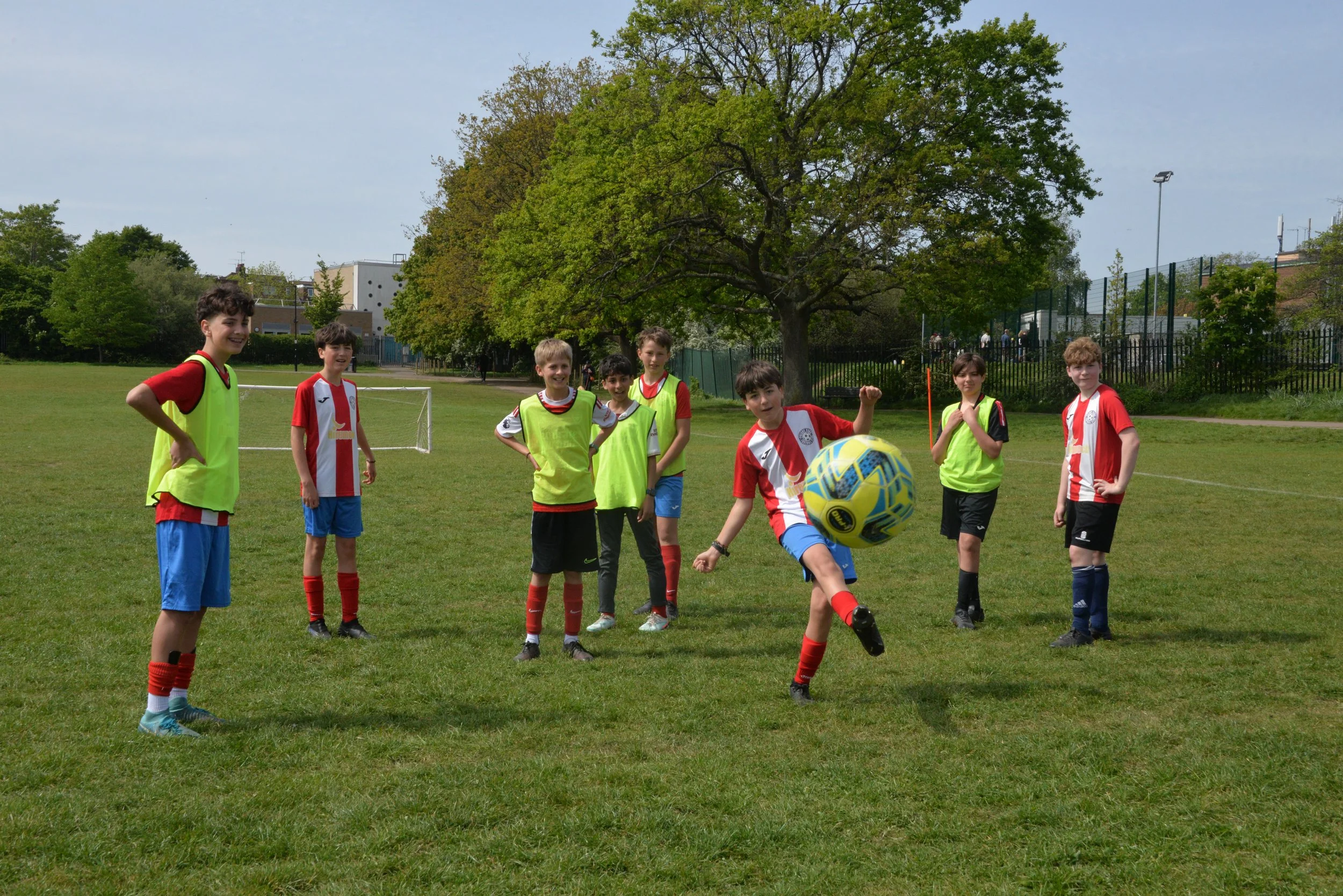 A group of children playing soccer outdoors on a grassy field on a sunny day. They are wearing colorful sports jerseys and soccer uniforms.