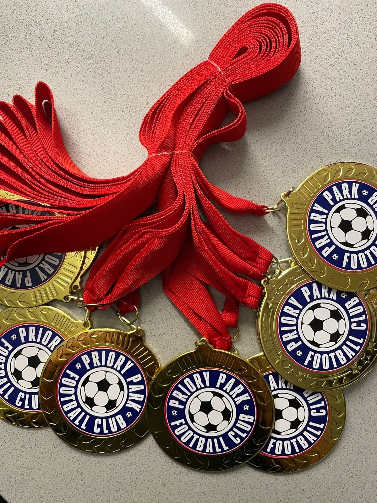 A collection of gold medals with red ribbons, each featuring a soccer ball and the text 'Priority Park Football Club'.