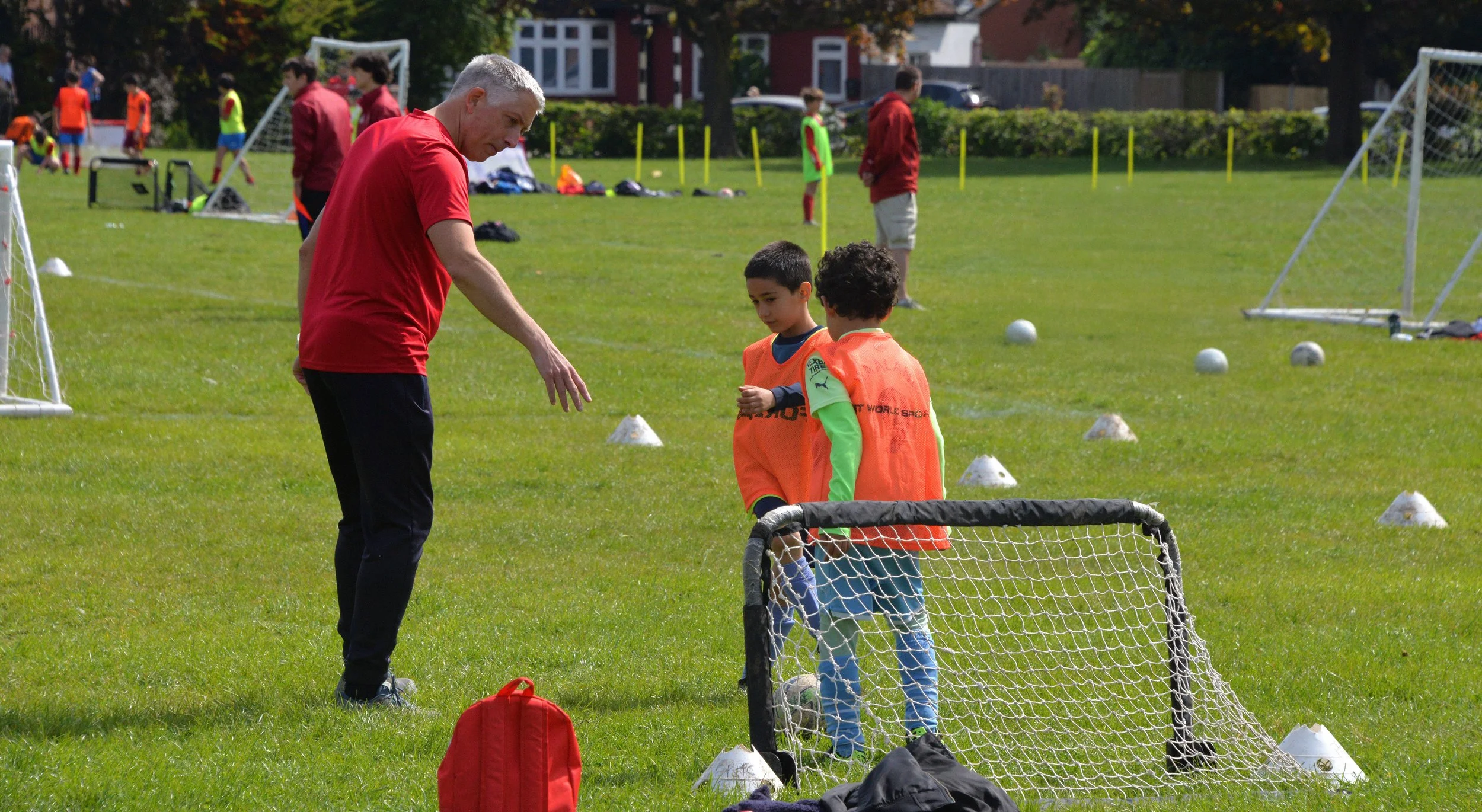 A youth soccer practice happening on a bright day in a grassy park, with children and adults participating and observing, playing soccer drills and engaging in organized activities.