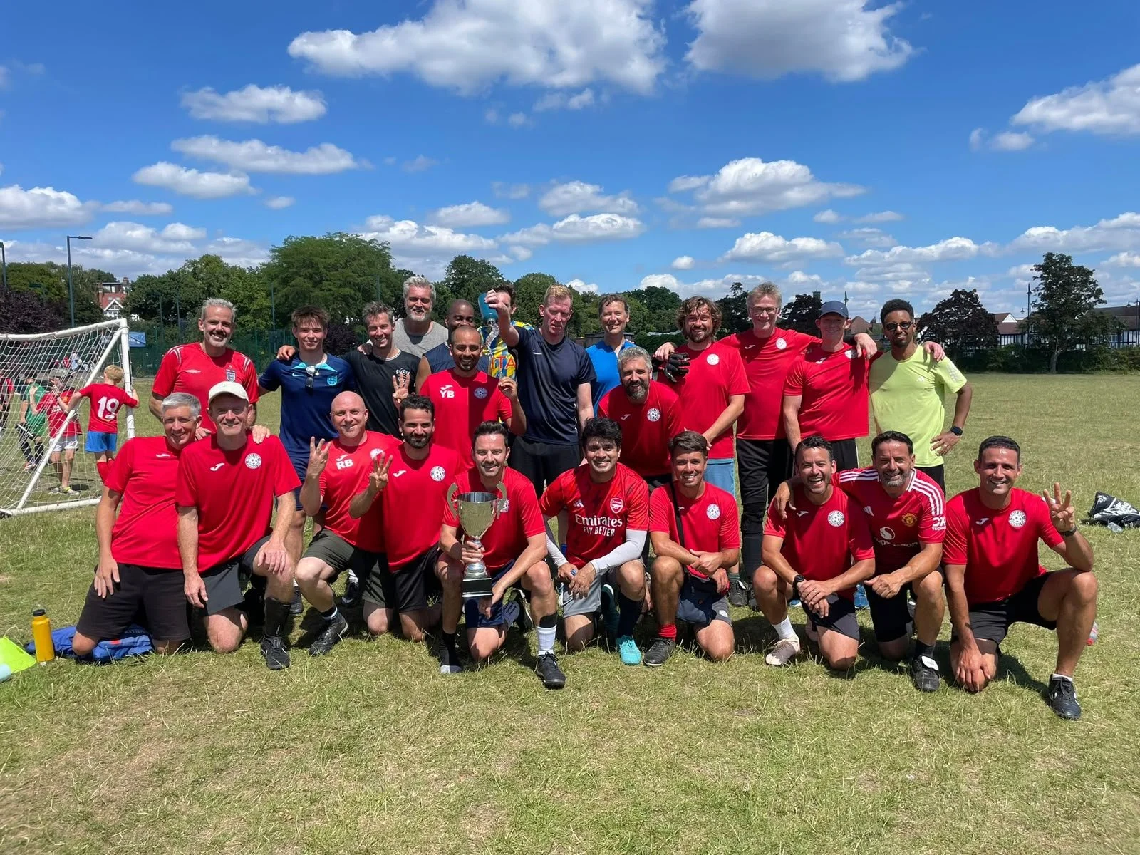 Group of people celebrating with a trophy on a soccer field on a sunny day.