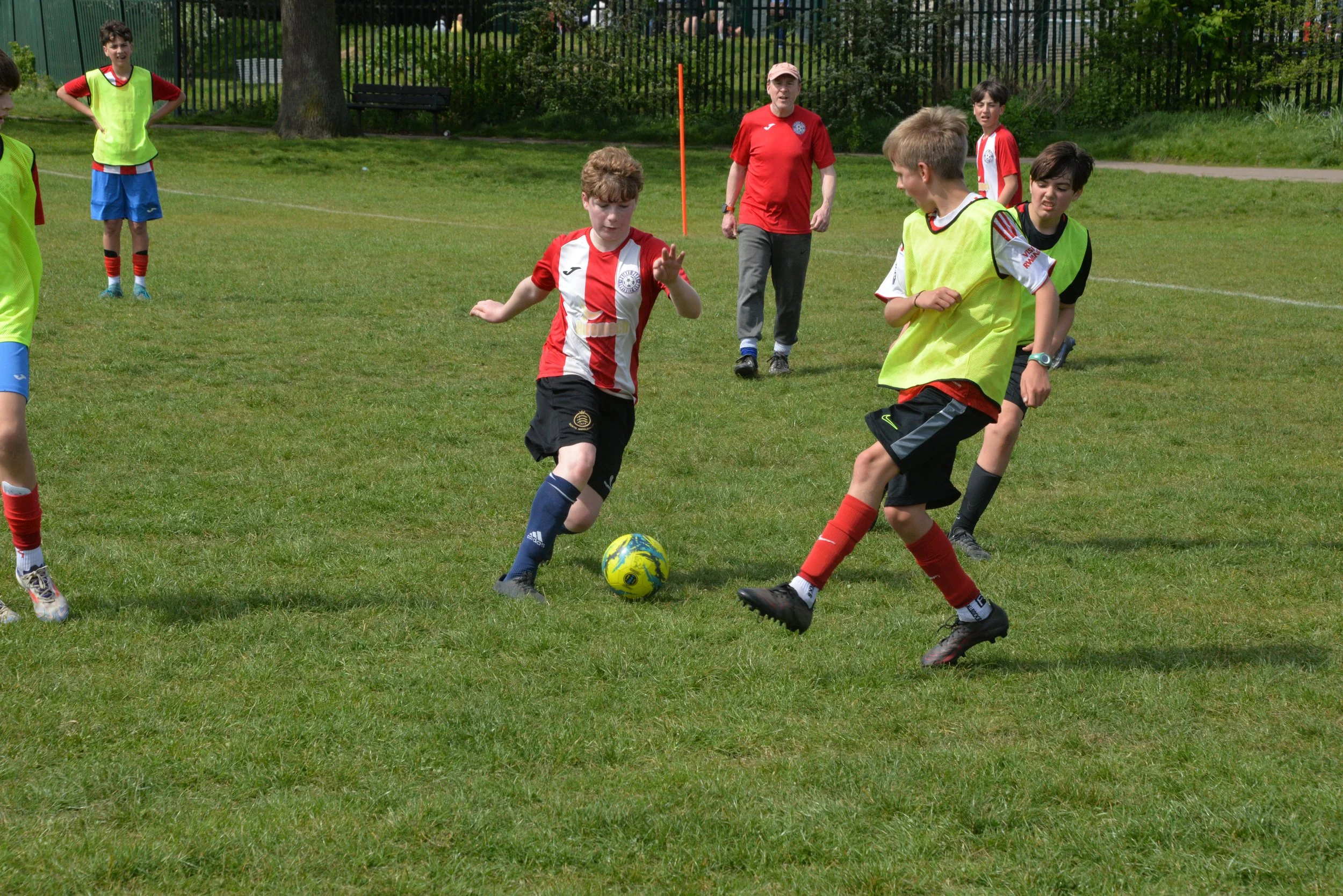 Children playing soccer on a grassy field with an adult coach watching.