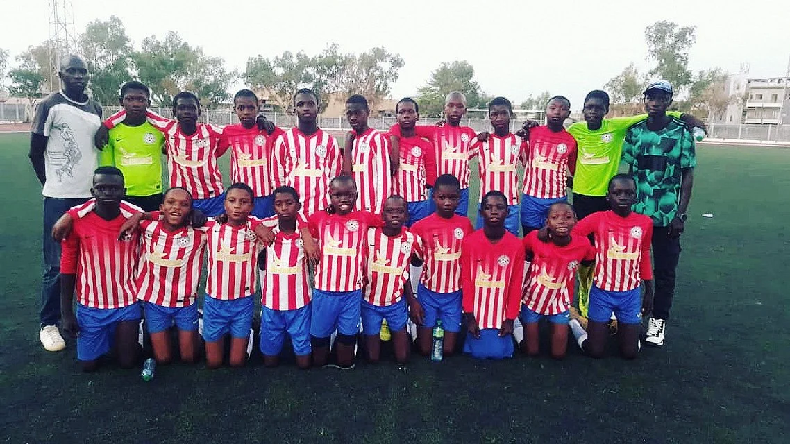 Group of young soccer players and coaches on a field, wearing red and white striped jerseys and blue shorts.
