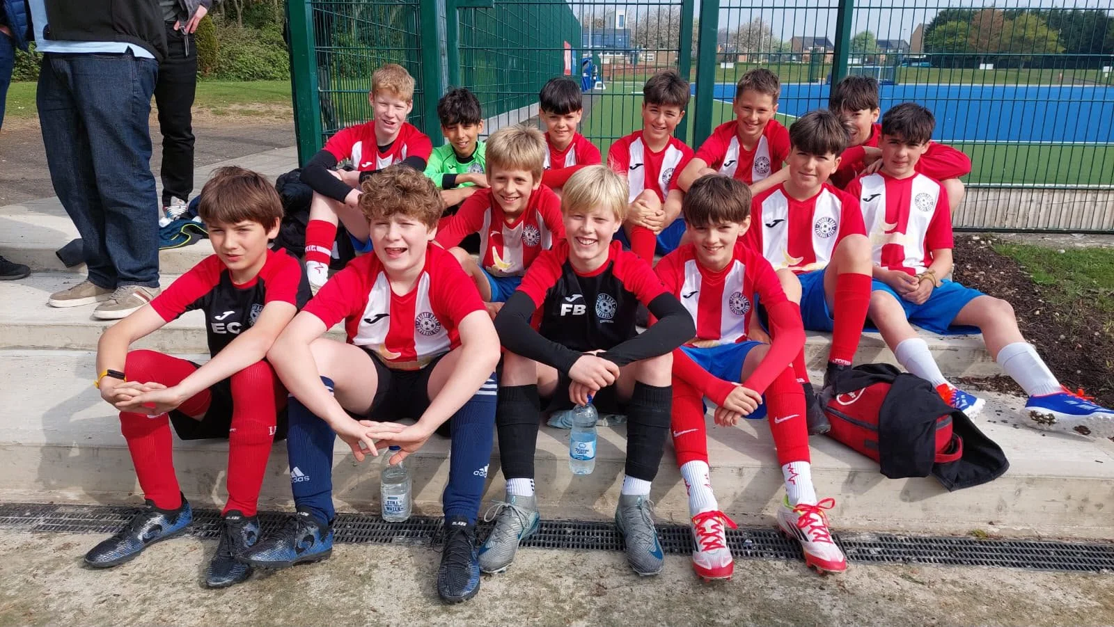 A group of young boys in soccer uniforms sitting on concrete steps after a game, with a soccer field in the background.