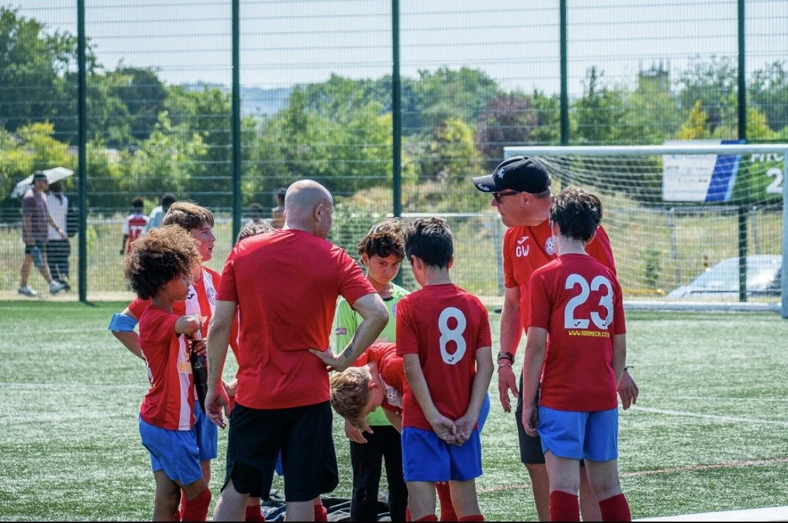 A youth soccer team gathered around their coach for a discussion on an outdoor field.
