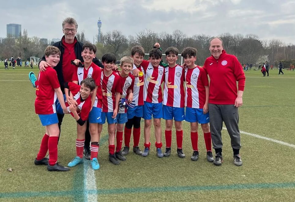 A youth soccer team with two adult coaches posing on a field, wearing red and white jerseys and blue shorts.