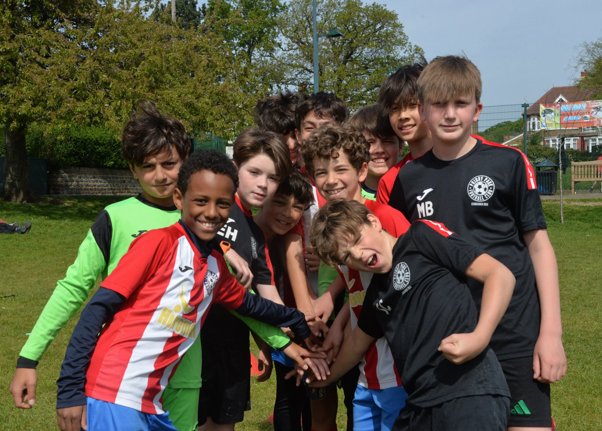Group of children dressed in soccer uniforms huddling together on a grassy field.