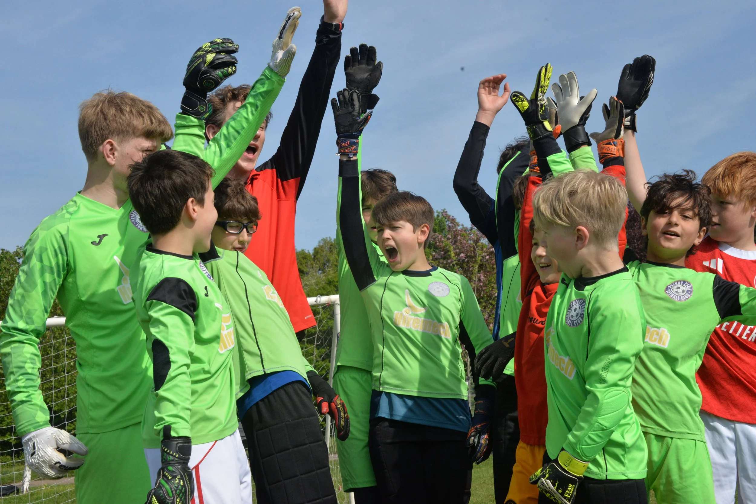 Group of young soccer players raising their hands in a team huddle on a sunny field.
