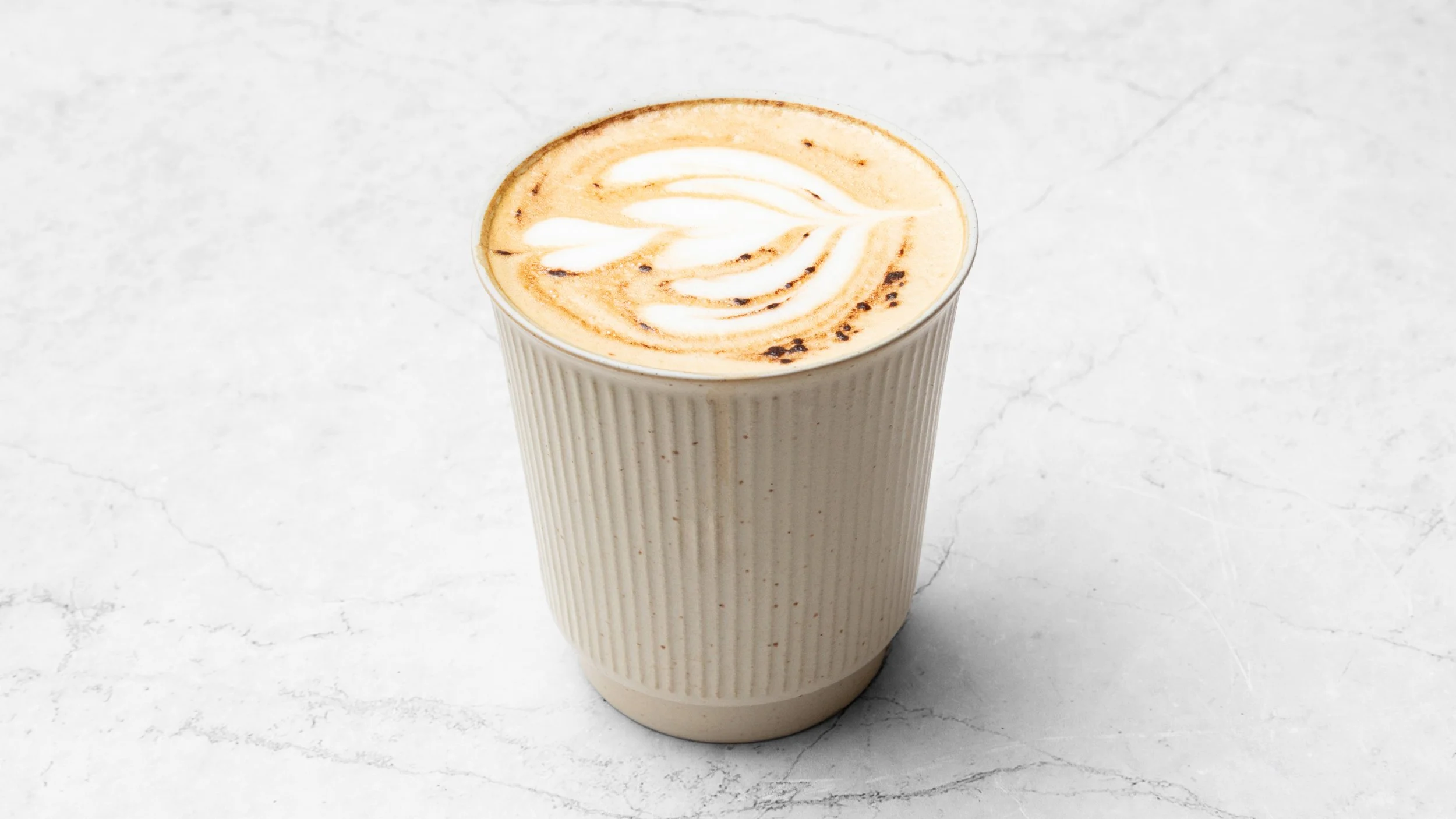 A cup of coffee with latte art on top, placed on a white textured surface.