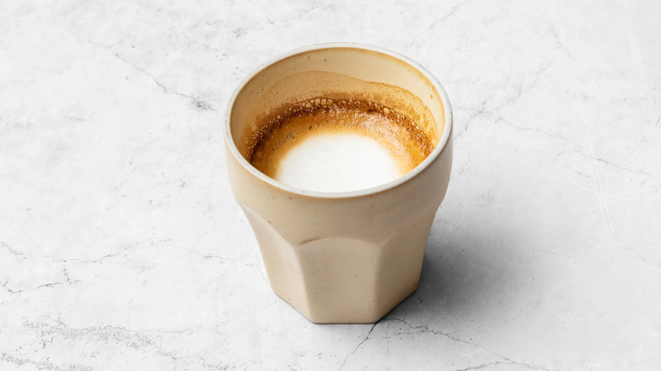 Empty beige coffee cup with remnants of coffee inside, on a white marble surface.