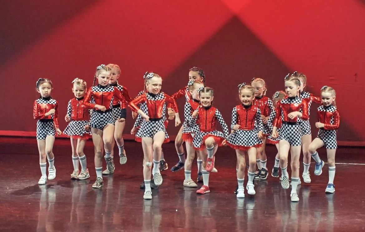 Young girls in red and black checkered dance costumes performing on stage.