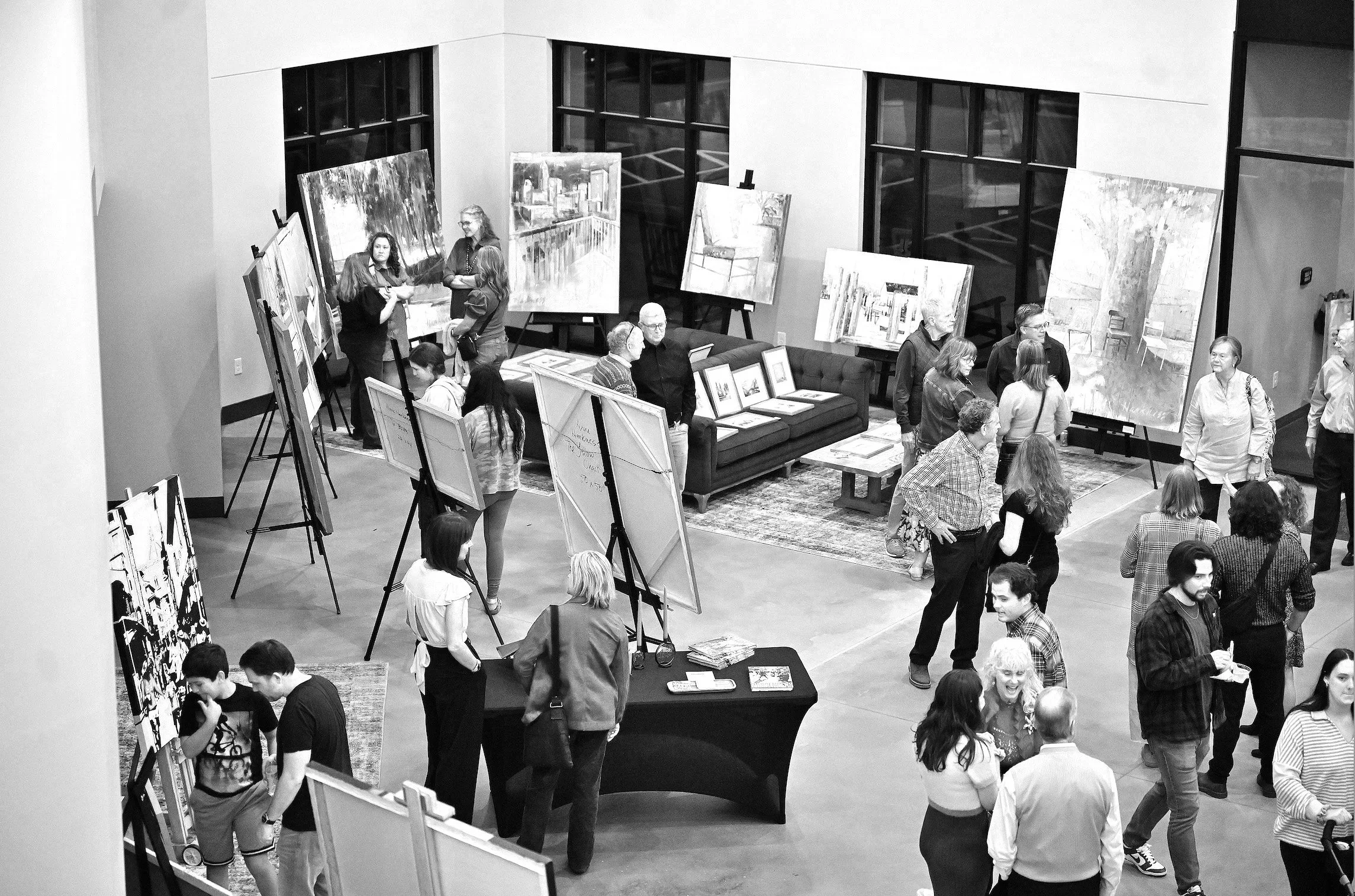People viewing and discussing paintings and artwork at an art exhibition in a gallery.