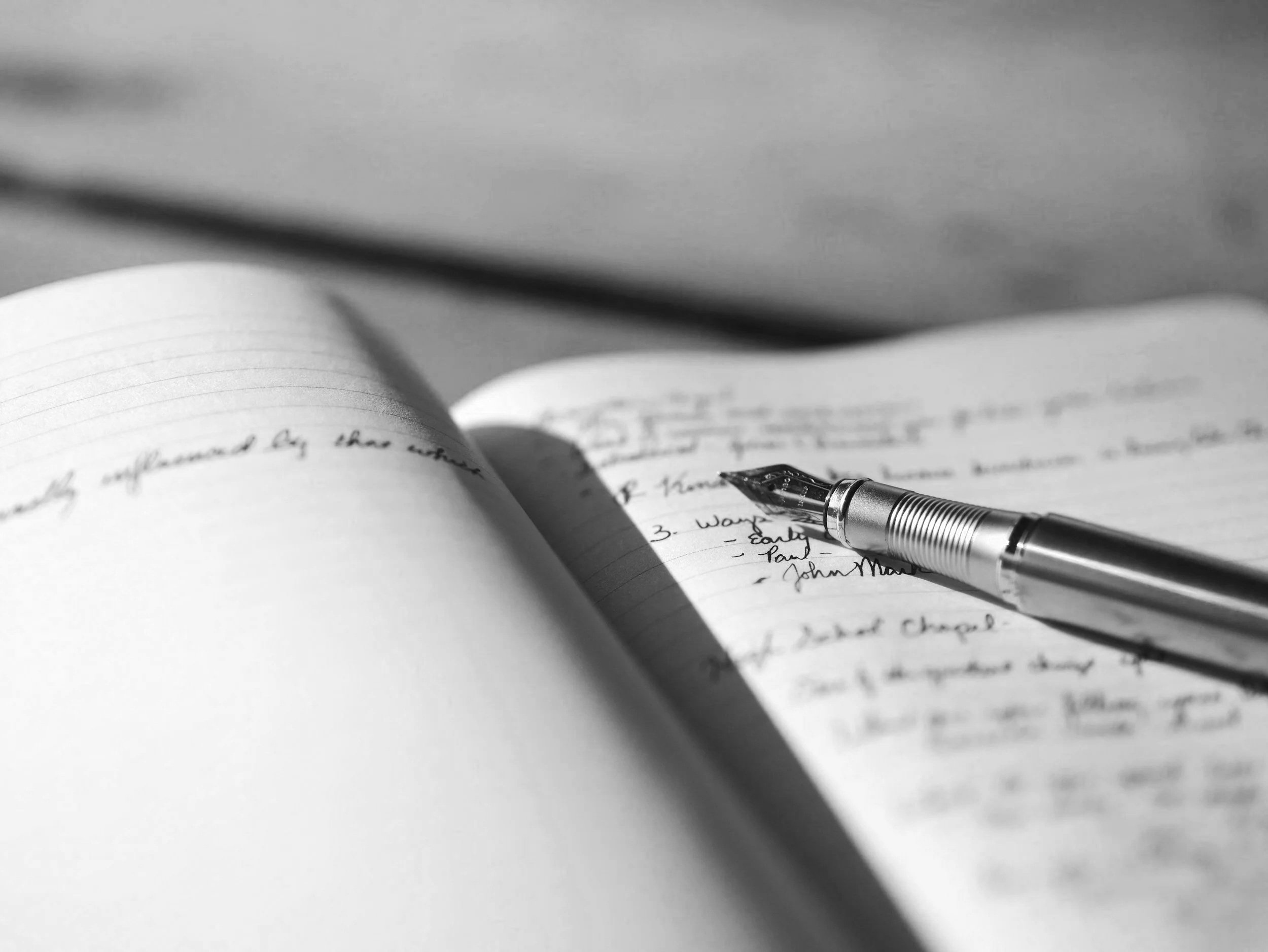Close-up of handwritten notes on lined paper with a black and silver fountain pen resting on the page, in black and white.