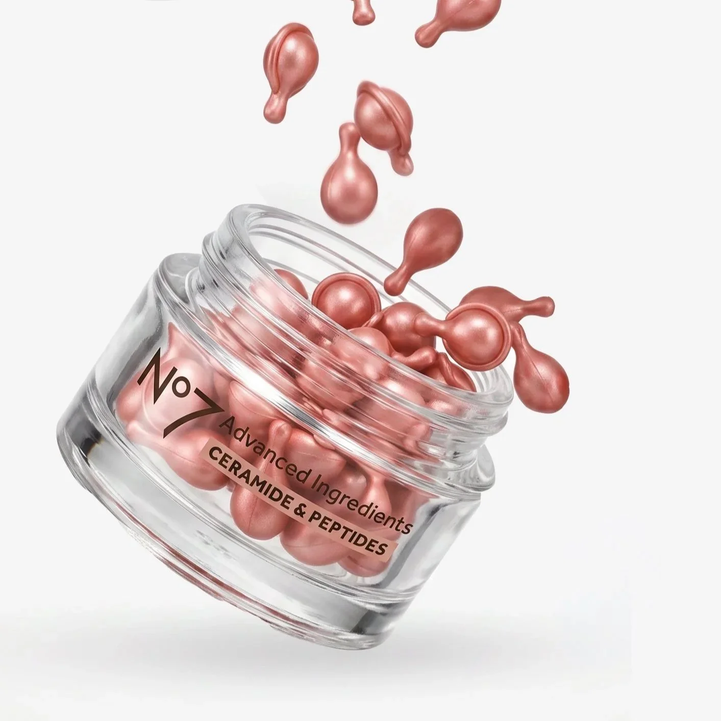 Close-up of a glass jar tilted, spilling pink capsules labeled 'No7 Advanced Ingredients Ceramide & Peptides' onto a white background.