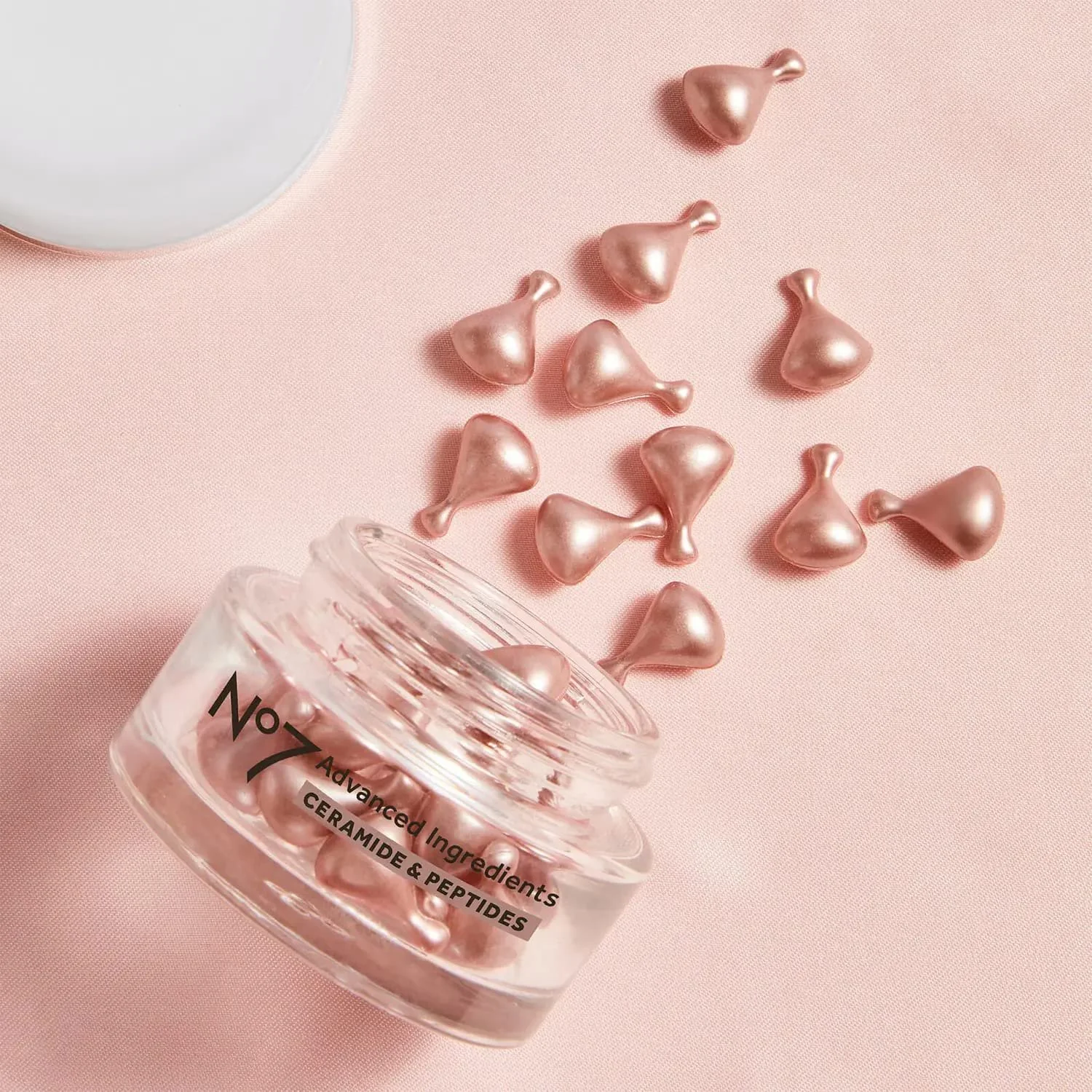 Pink collagen and peptide supplement capsules spilled from a clear jar onto a pink surface with a white container partially visible at the top.