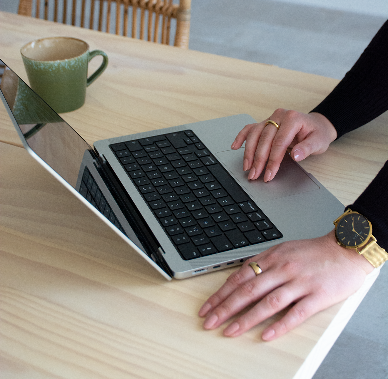 Persoon typt op een laptop op een houten tafel met een groene kop koffie erbij.