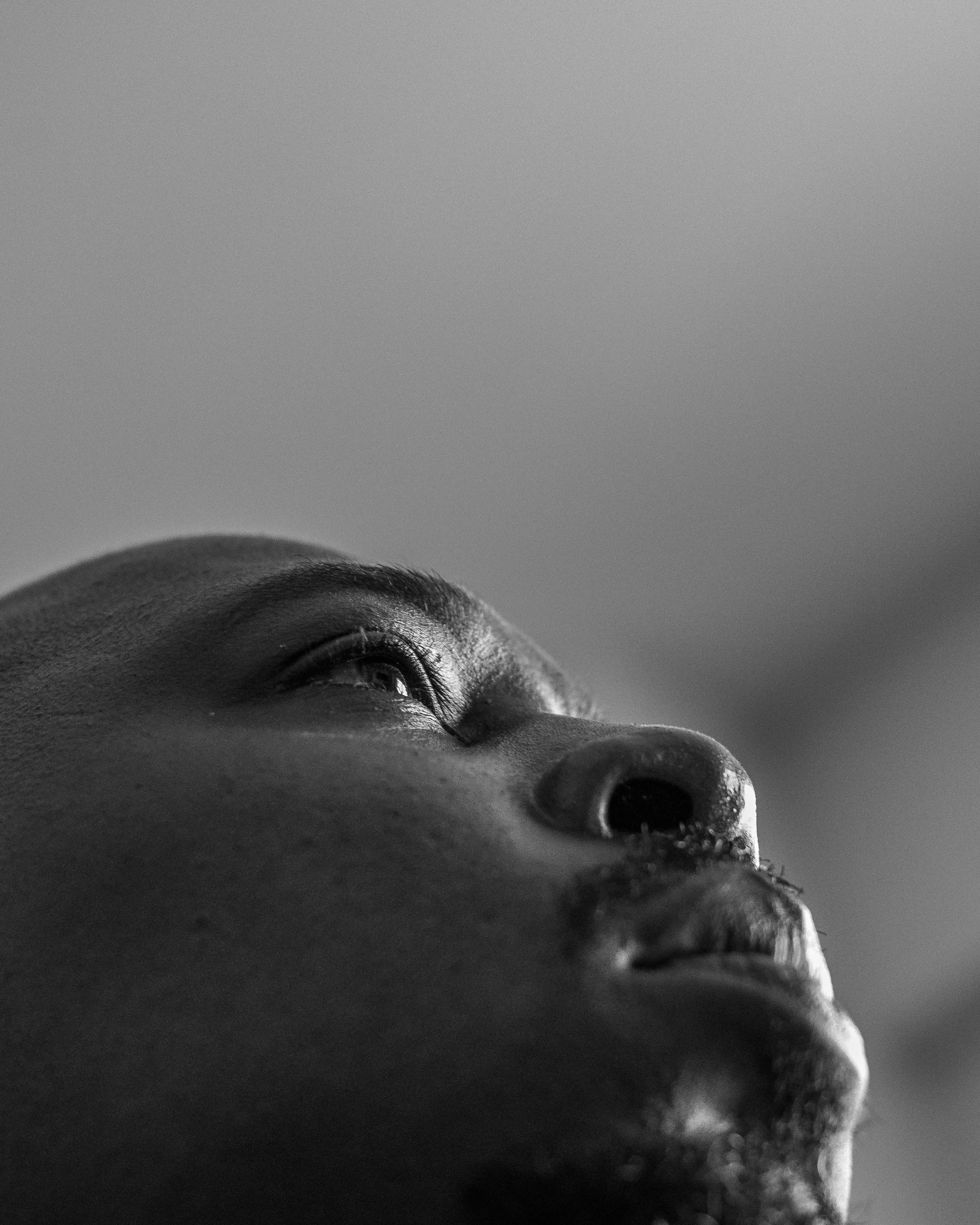 Close-up black and white photo of a person's nose and eye, with the head tilted back and the face partially visible against a plain background.