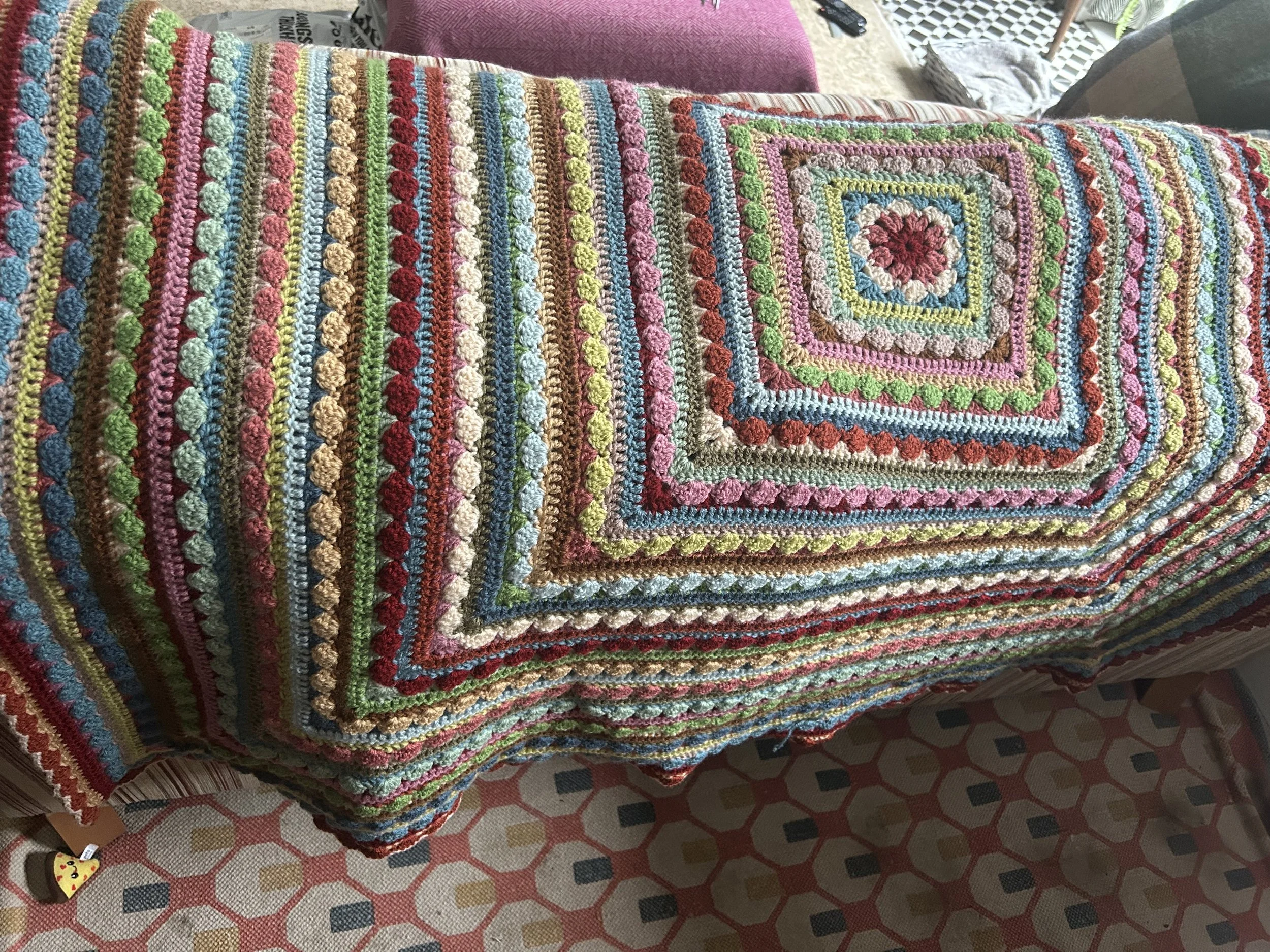 Stack of folded colorful crochet blankets placed on a table with patterned tablecloth.