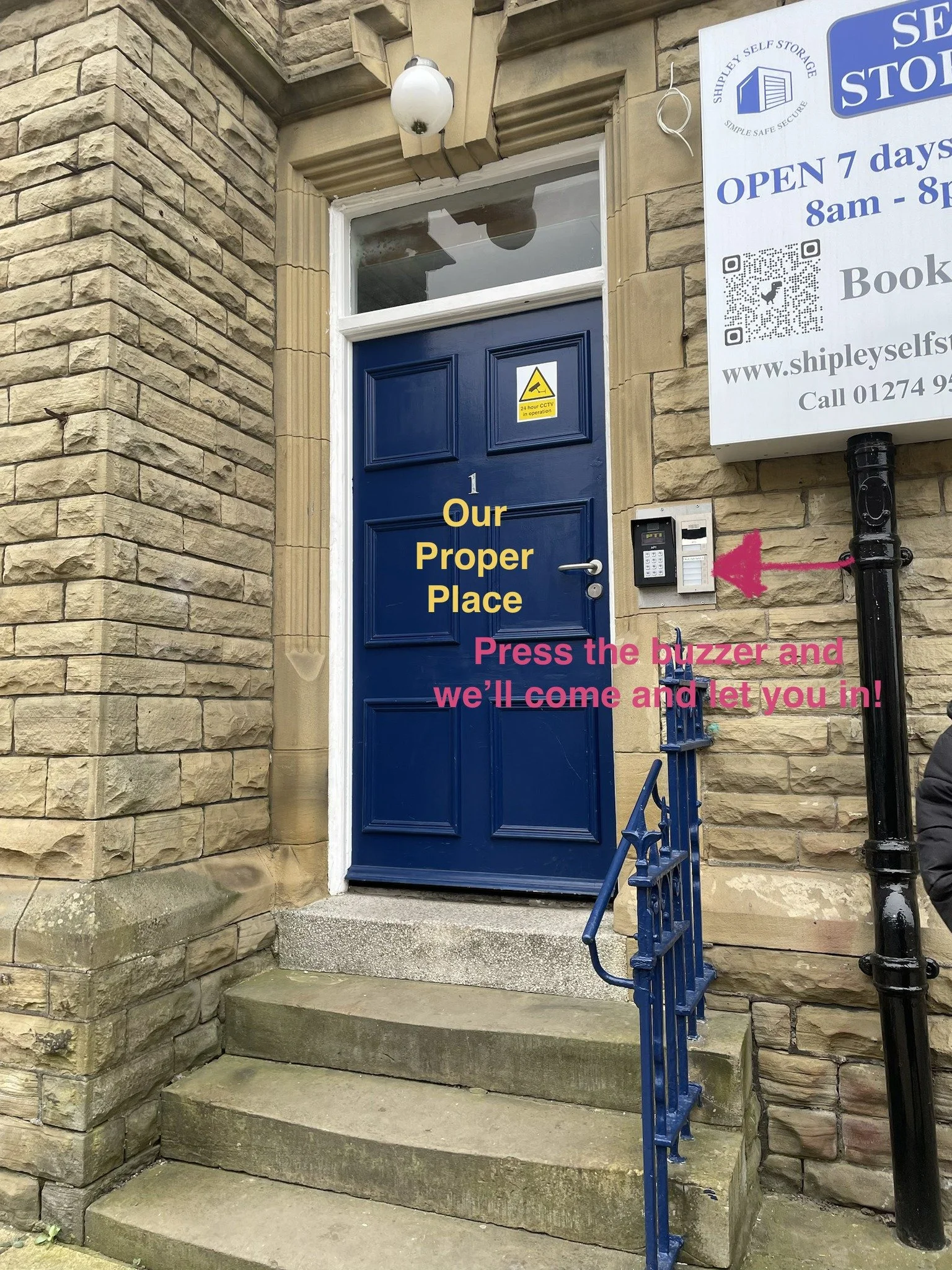 Blue door with welcome sign on it, surrounded by stone walls and stairs, with a security keypad and a sign indicating CCTV operation outside.