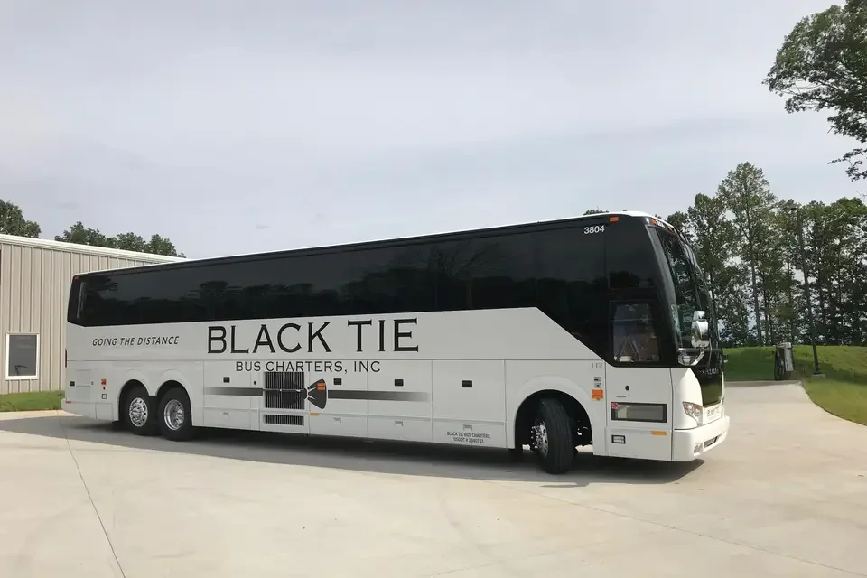 Black Tie Bus Charters, Inc. bus on a parking lot with trees and a building in the background.