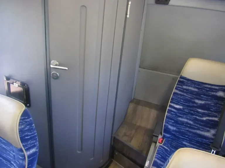 Interior of a train with blue patterned seats, a closed gray door, and a wooden step or small platform.