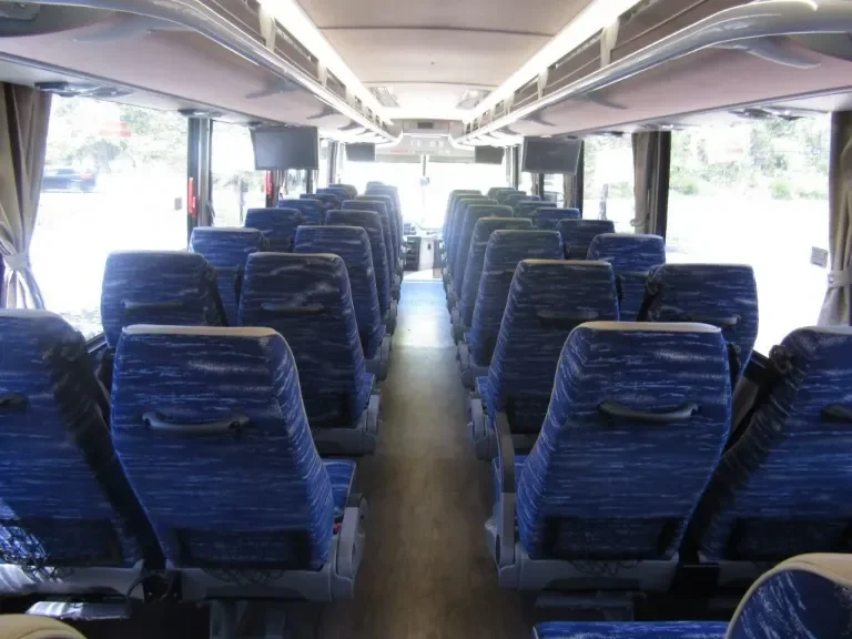 Inside of an empty tour bus with blue patterned seats and windows on both sides.
