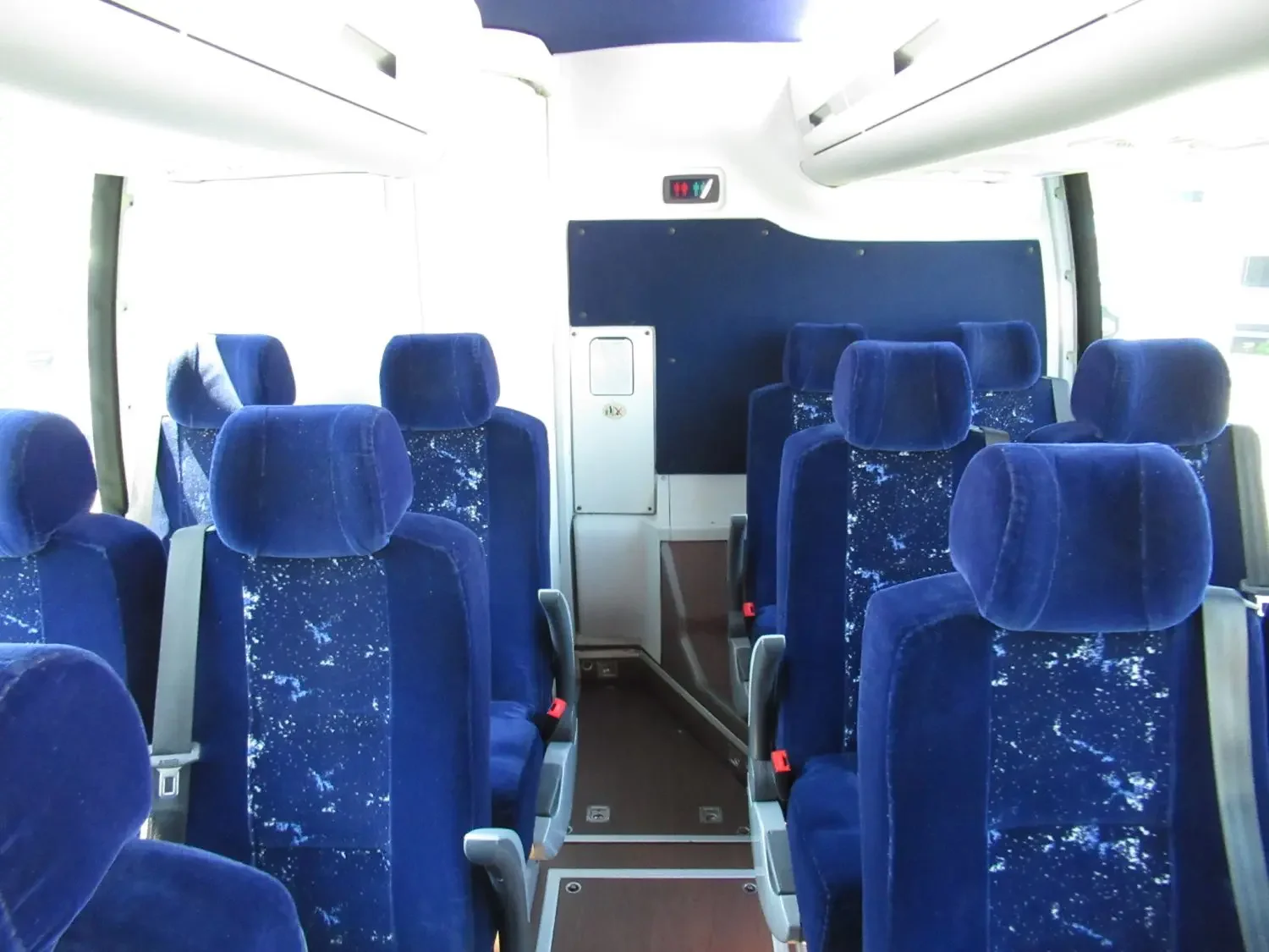 Interior of an empty bus with blue velvet seats, large windows, and an overhead sign indicating gendered restroom facilities.