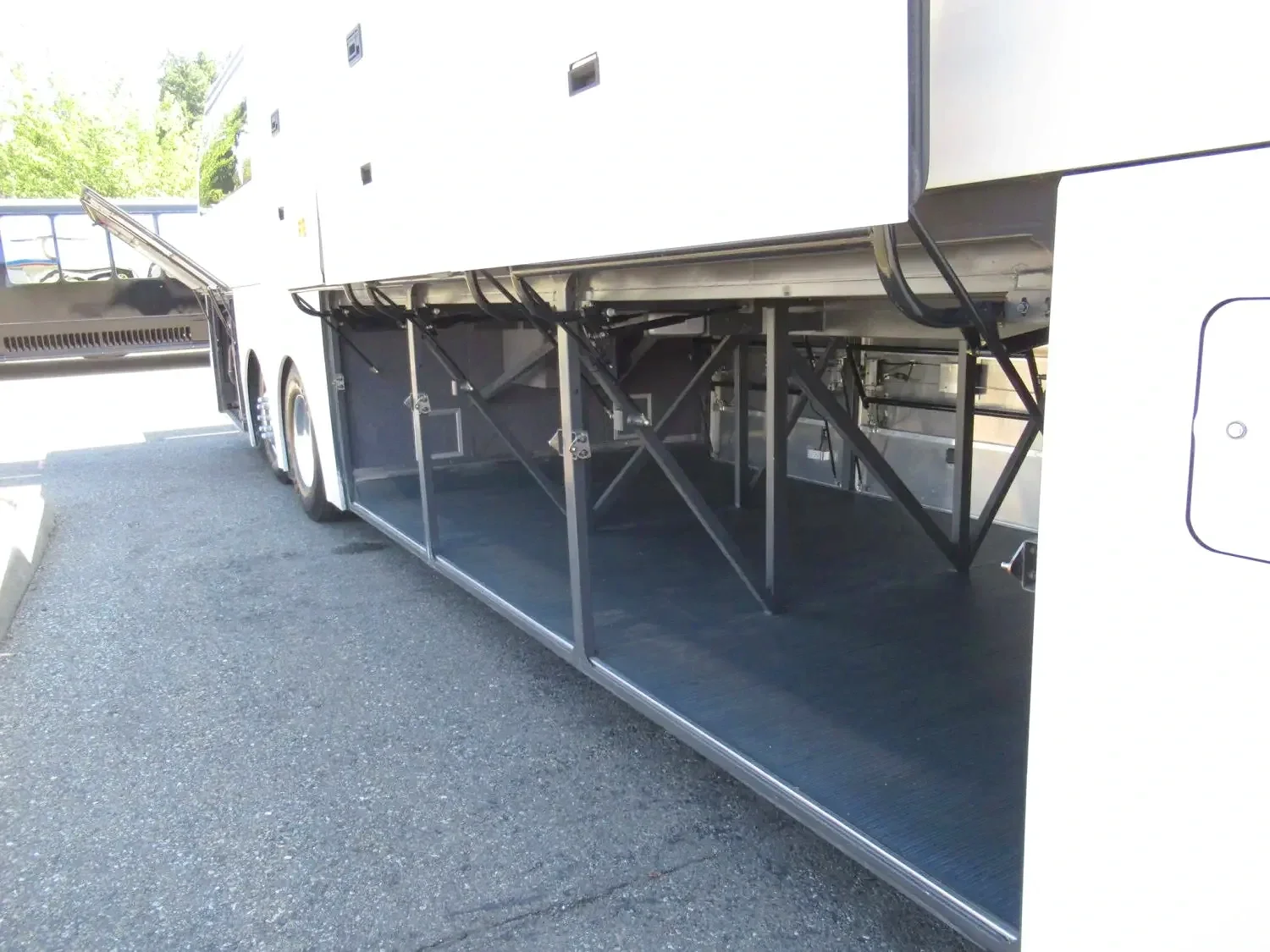 Empty storage compartment under a large white bus, with a metal frame for luggage or cargo, parked on asphalt.