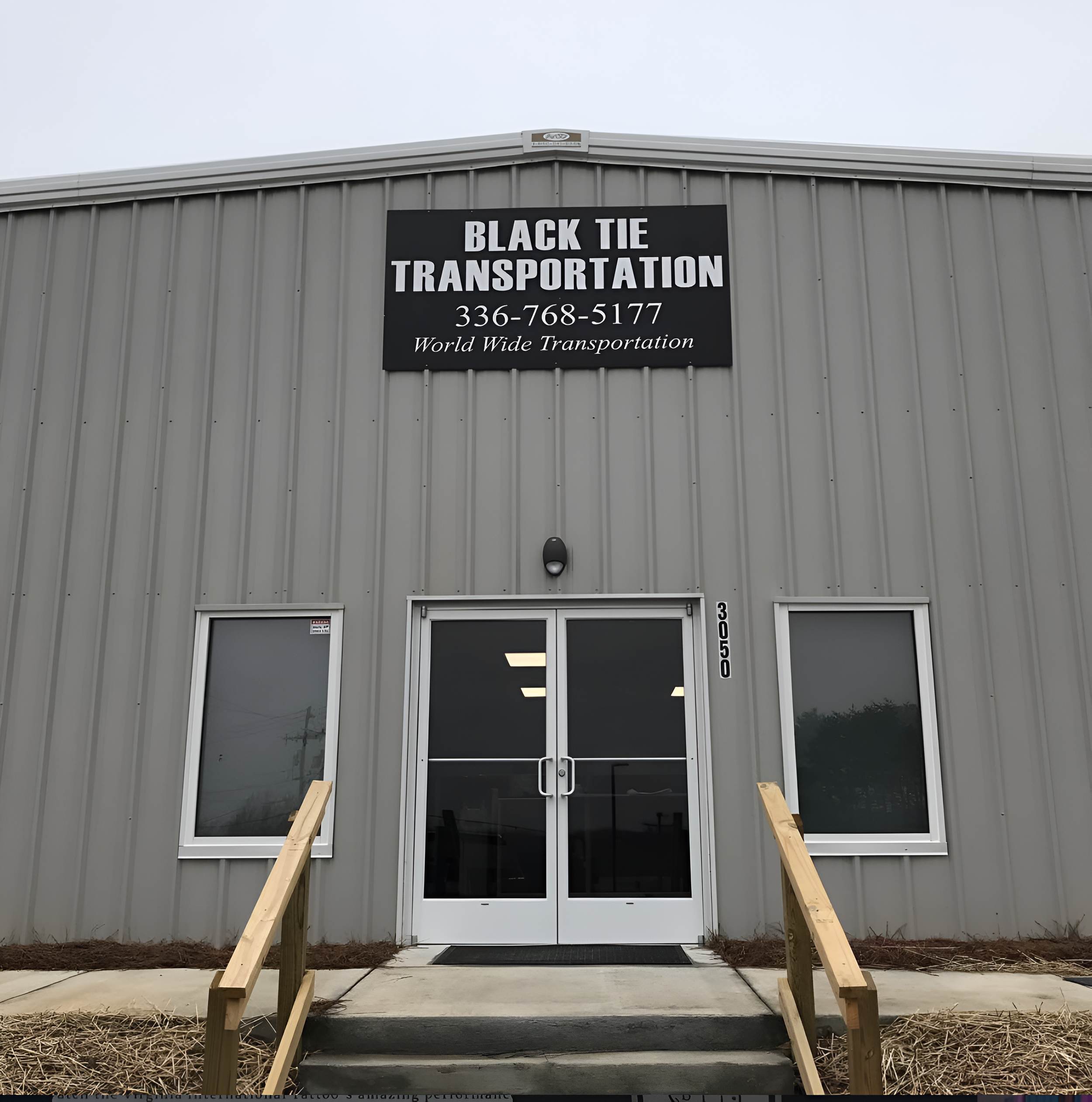 Black Tie Transportation and Bus Charters headquarters, with a sign that reads "Black Tie Transportation" and a phone number, featuring stairs leading up to the entrance, and a grey exterior.