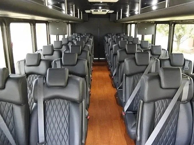 Interior of a bus with multiple rows of black leather seats, seatbelts, and windows on both sides.