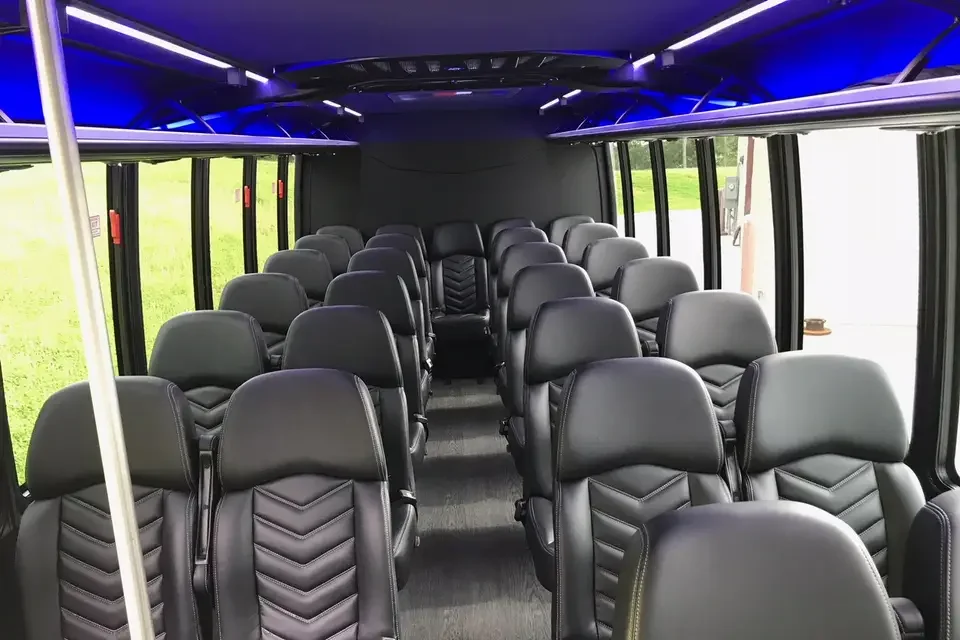 Interior of a bus with multiple rows of black leather seats and large windows on both sides, illuminated by blue lighting on the ceiling.