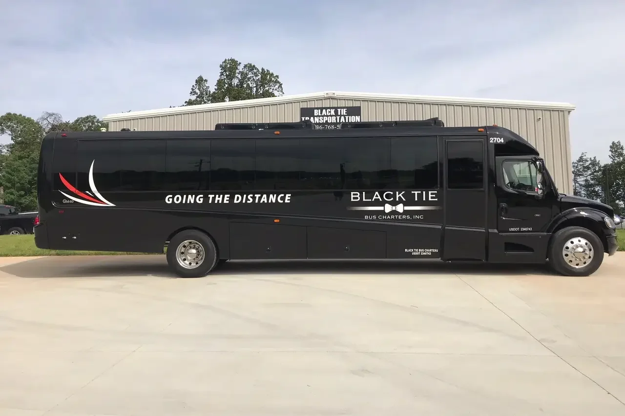 Black bus with the text 'Going the Distance,' 'Black Tie,' and 'Bus Charters, Inc.' parked outside a beige building with trees in the background.
