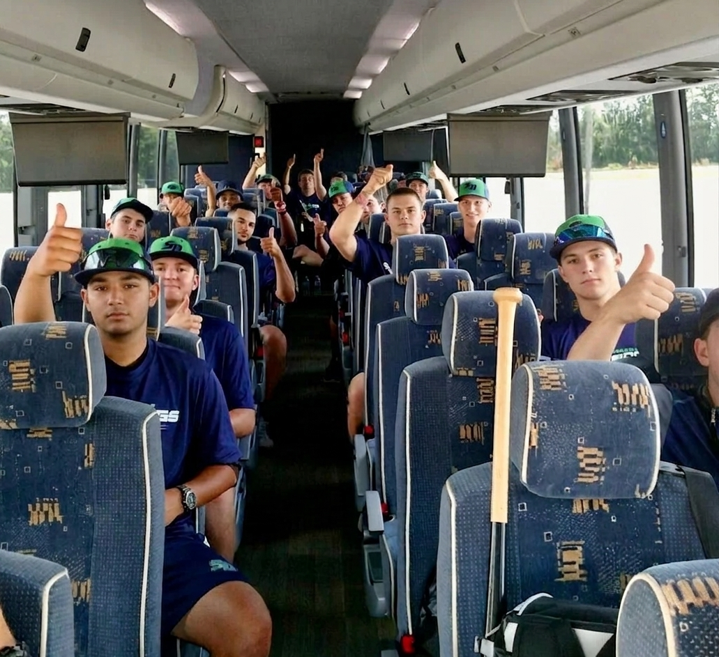 A group of young men sitting in a bus, giving thumbs-up and looking at the camera, some wearing green caps and sunglasses, with water bodies visible through the windows.
