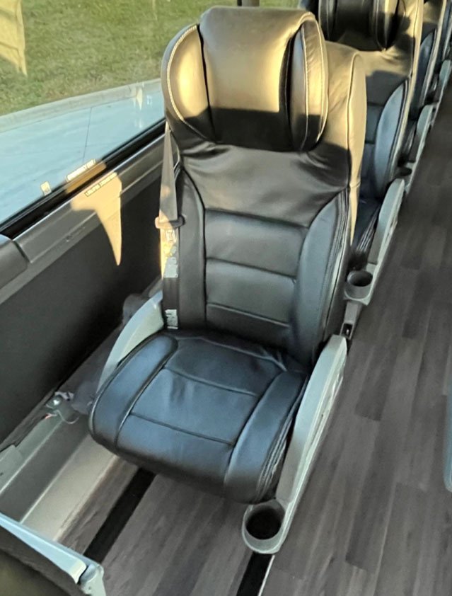 A black leather passenger seat on a bus or train, positioned next to a window with sunlight.