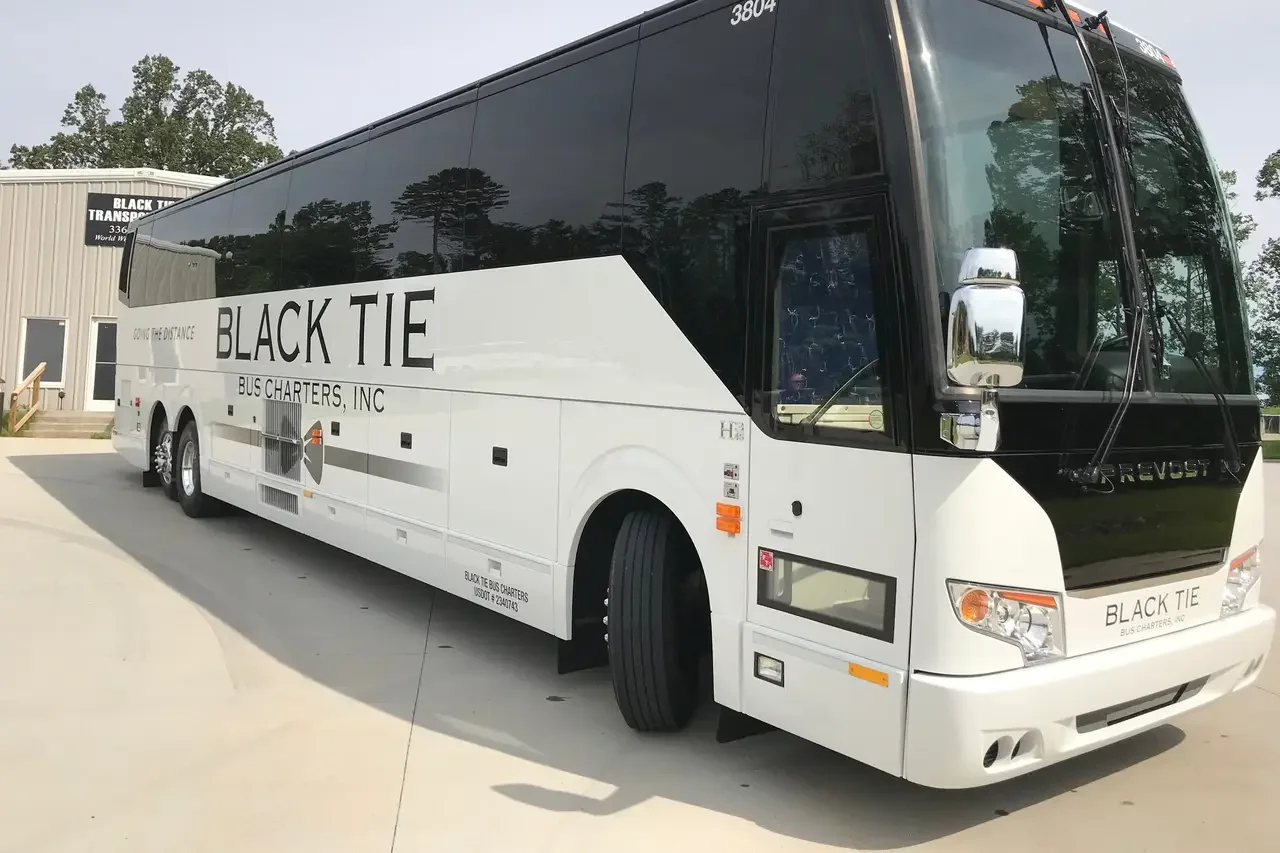 White and black bus with the words "Black Tie Bus Charters, Inc" painted on the side, parked outside a building.